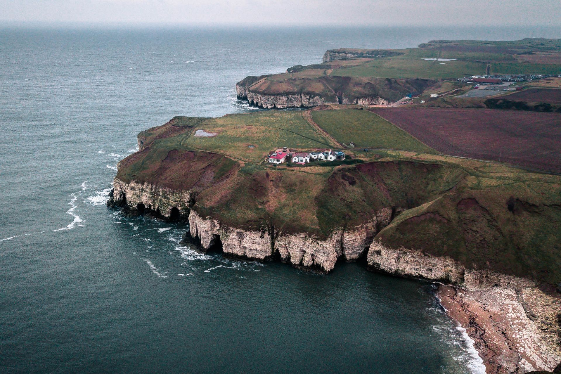 houses-sitting-on-edge-of-cliff-by-the-sea-on-a-dark-moody-autumn-winter-day-in-britain-at-flamborough-head
